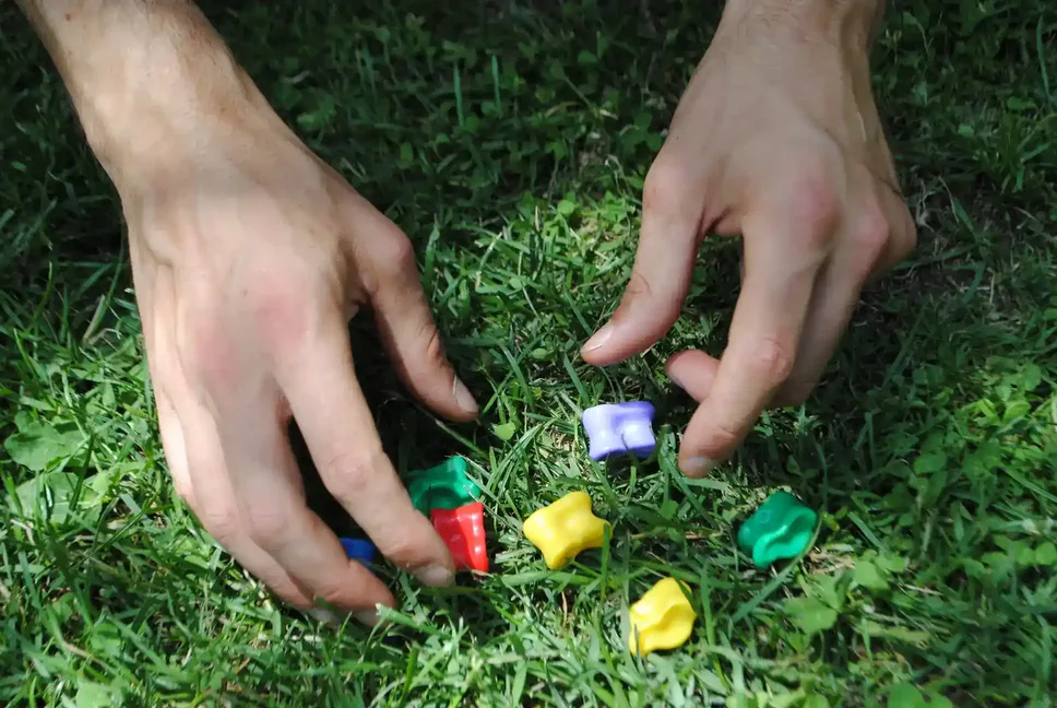 Unas manos jugando a las tabas de colores en un fondo de césped.