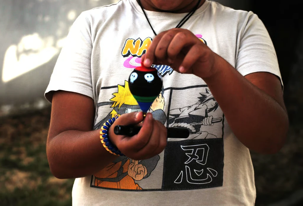 Fotografía de cerca de las manos de un niño mostrando su peonza negra con calaveras.